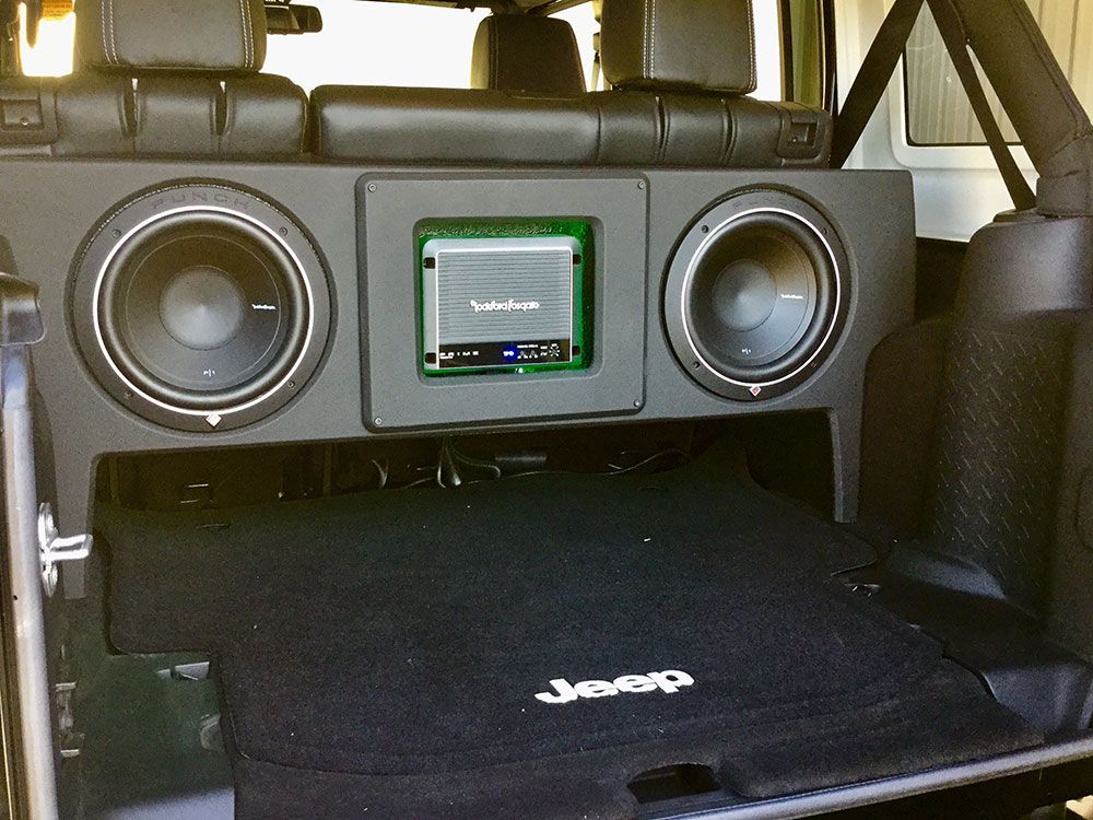 Custom car audio system installed in a Jeep: two subwoofers, an amplifier, and a storage compartment.