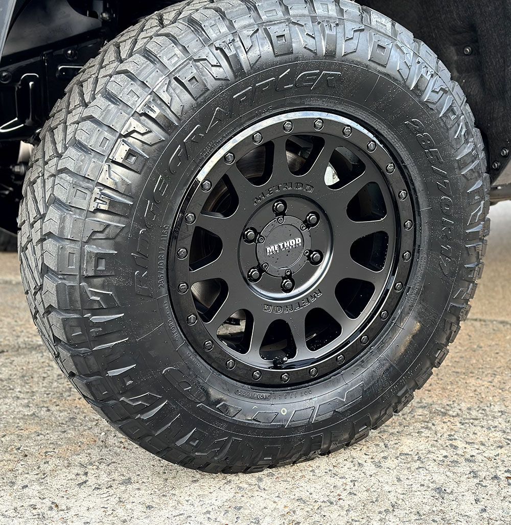 Black off-road tire on a black wheel, wet, close-up, on concrete.