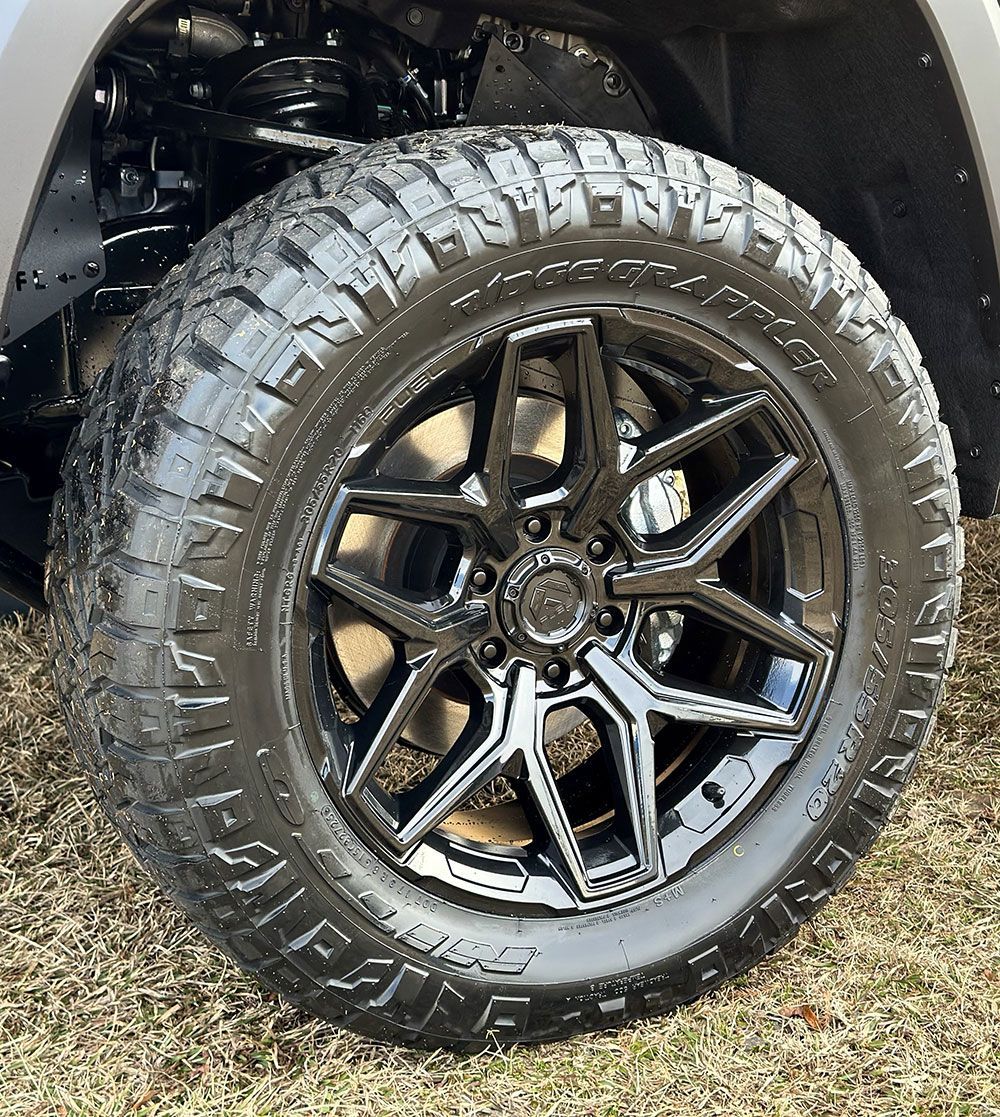 Black alloy wheel with all-terrain tire on a truck, with a muddy appearance.