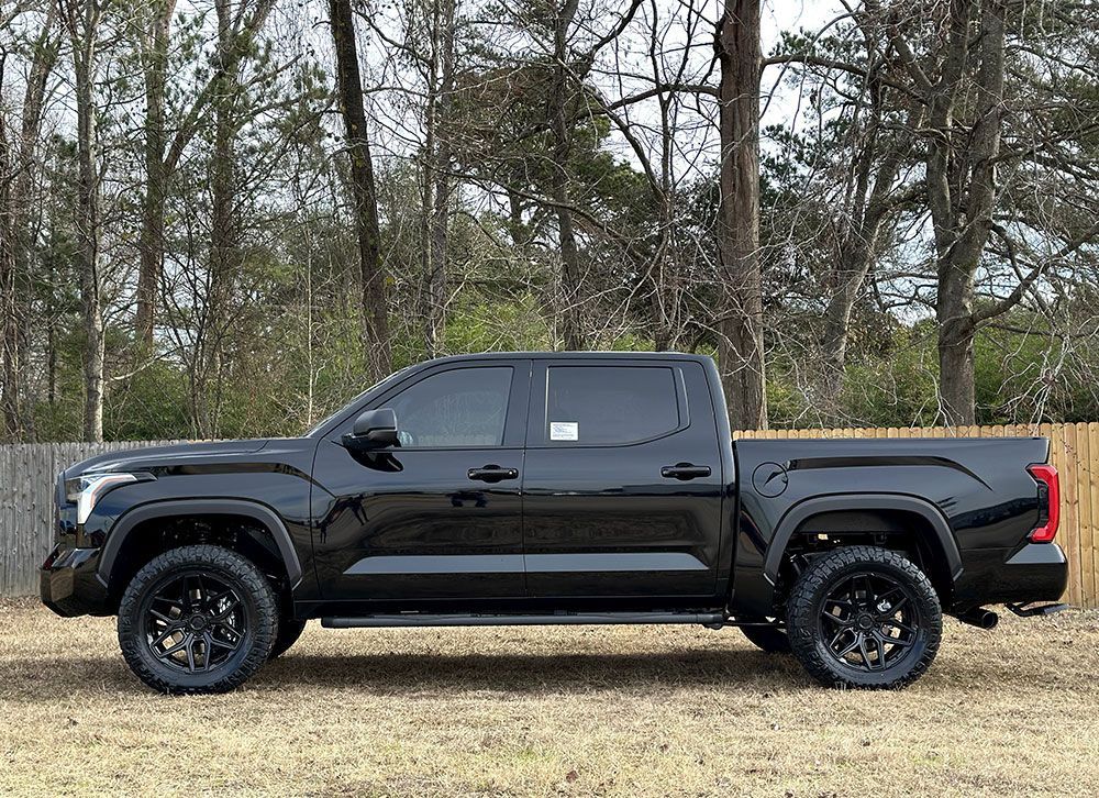 Black Toyota Tundra pickup truck parked outdoors, black wheels, dark tinted windows.