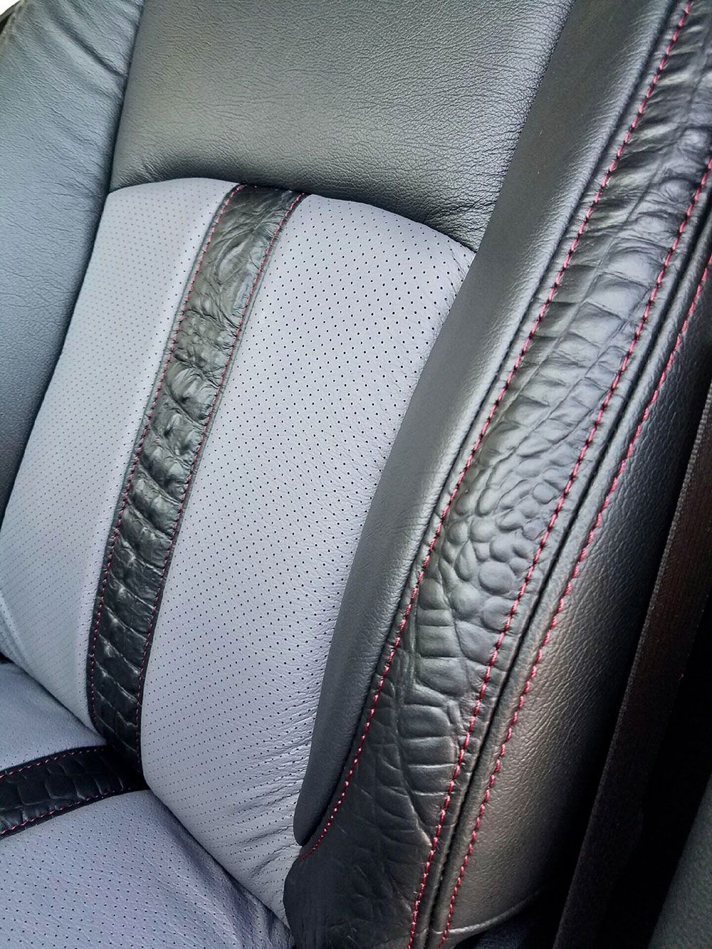 Close-up of a car seat. Black and gray leather with red stitching. Perforated gray center panel.