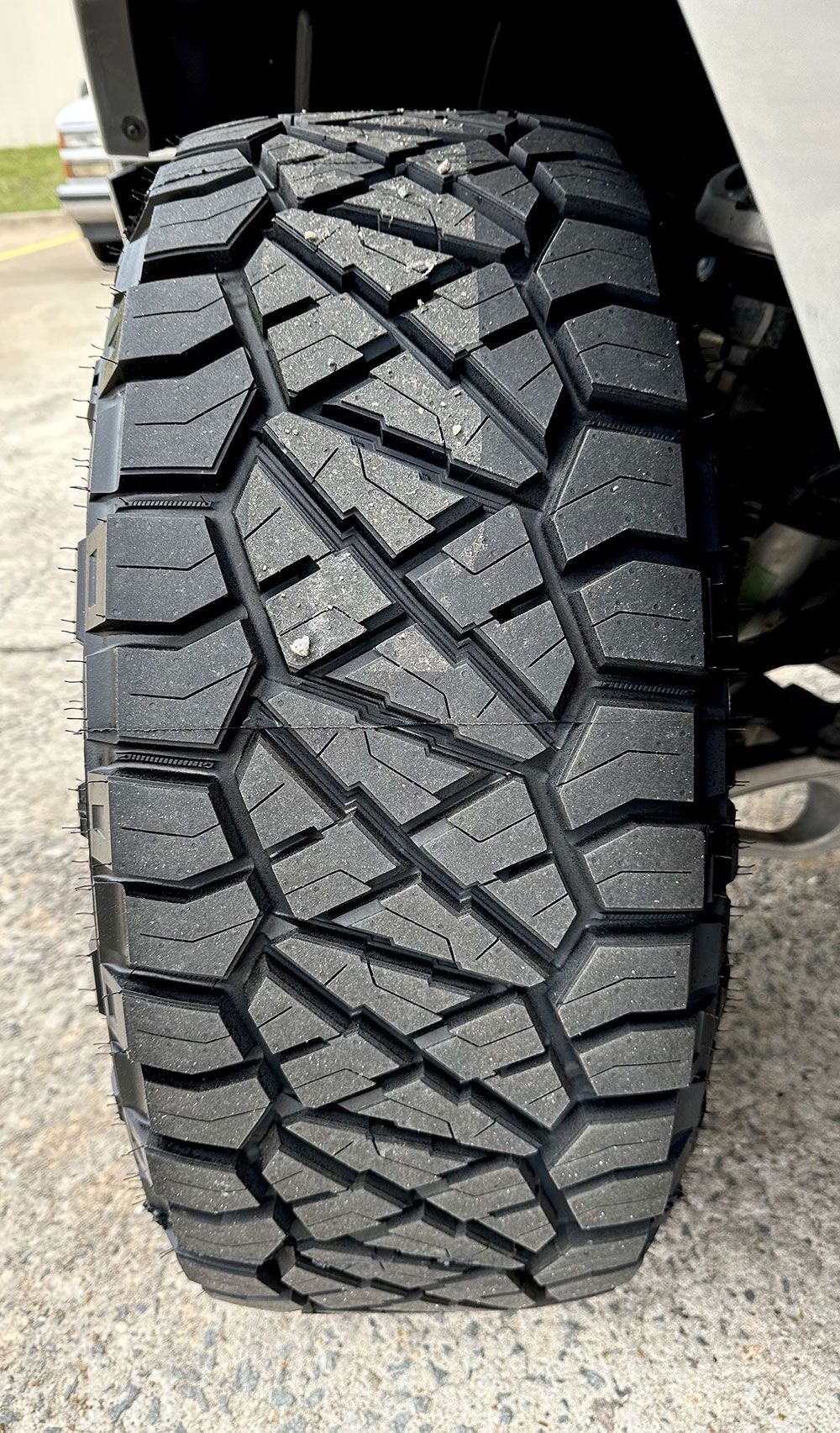Close-up of a black off-road tire on a vehicle, showing aggressive tread pattern and side view.