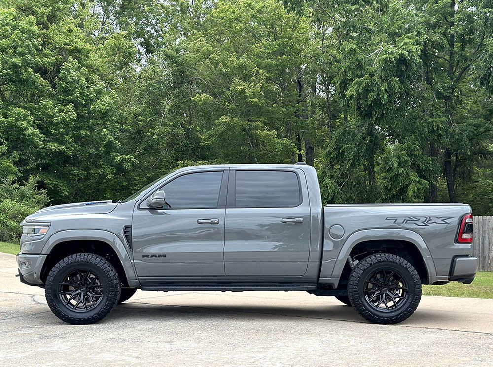 Gray Ram truck with black wheels parked on a paved surface, trees in the background.