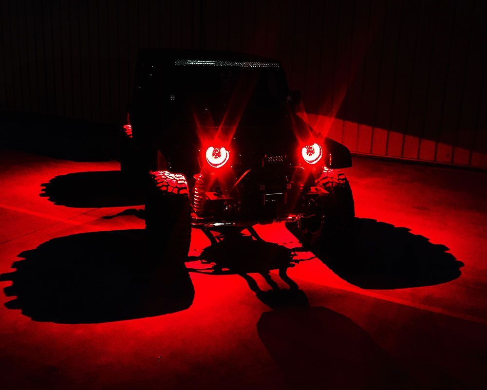 Black Jeep with red headlights casting long shadows on a red surface at night.