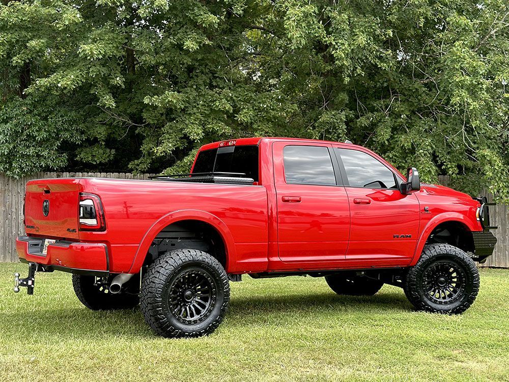 Red lifted pickup truck on grass with black wheels, tinted windows, and a black front bumper.
