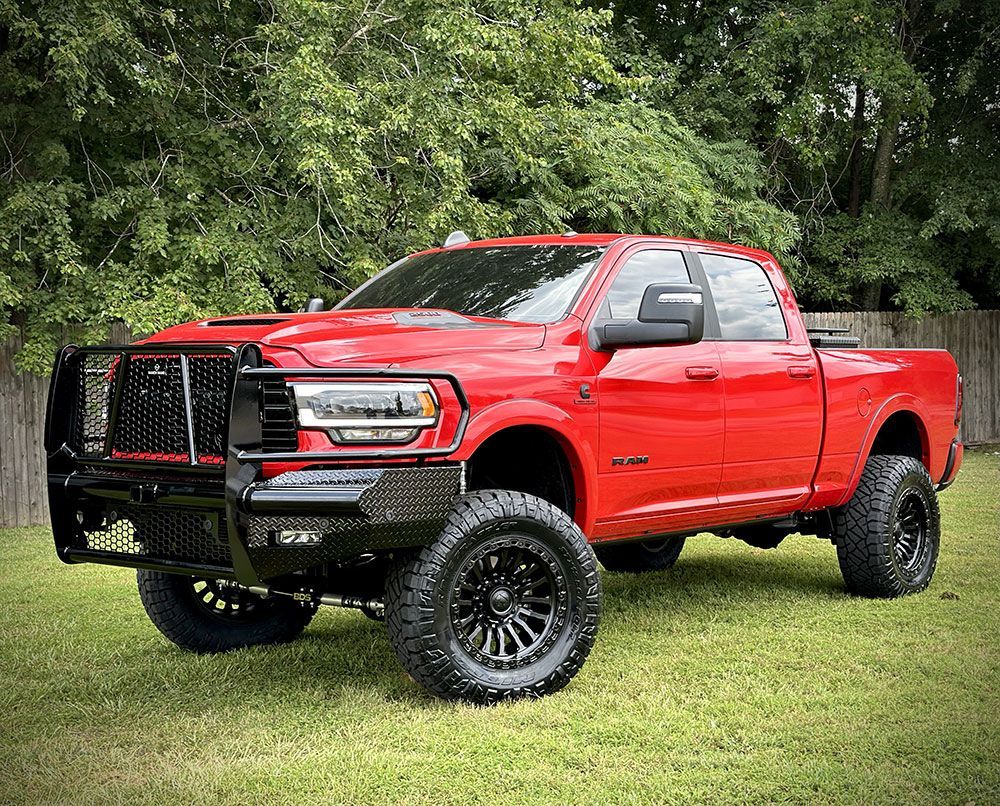 Red Ram truck with black accents, sitting on a grassy lawn with trees in the background.