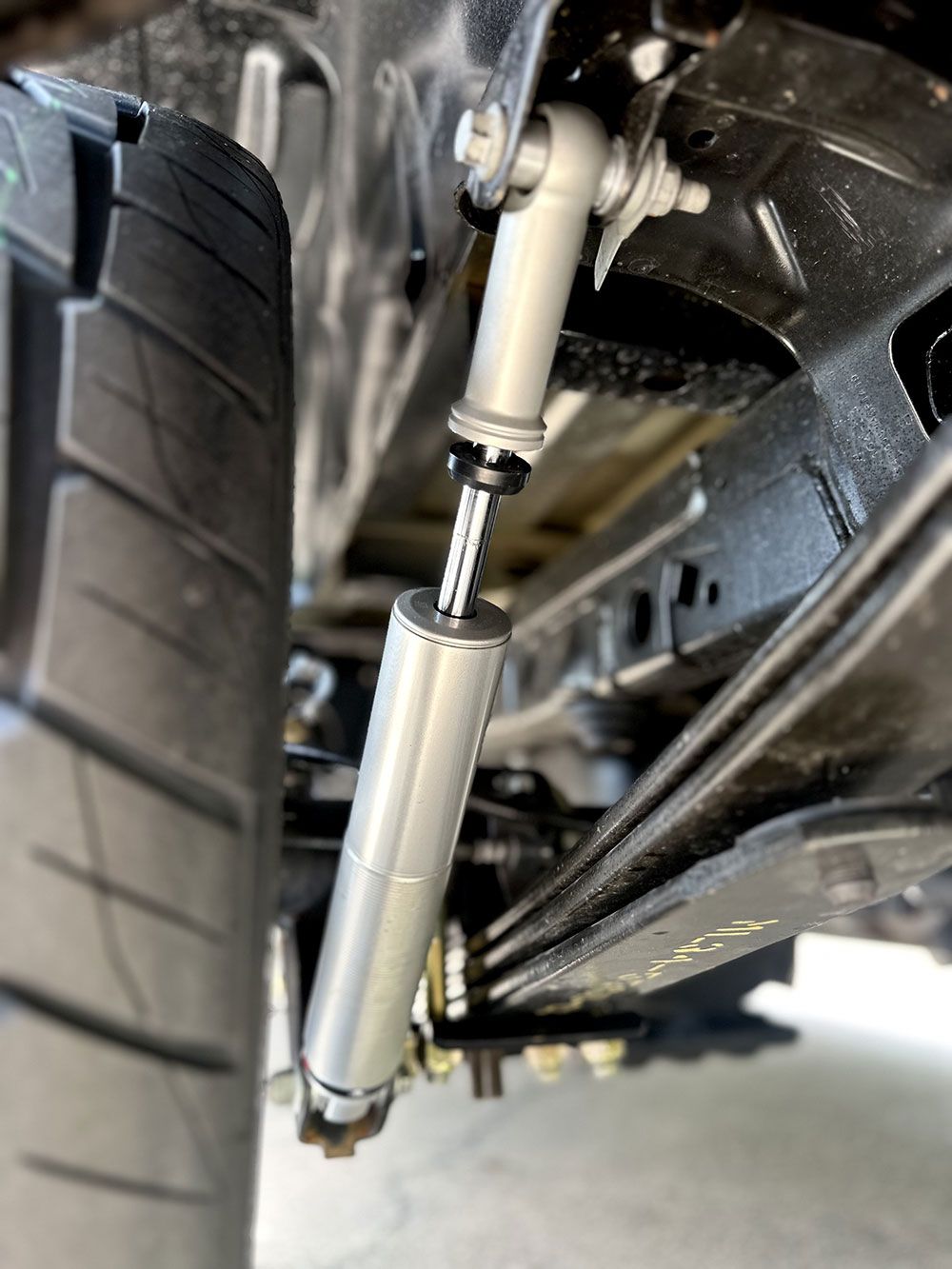 Silver shock absorber installed on a vehicle's undercarriage near a tire.