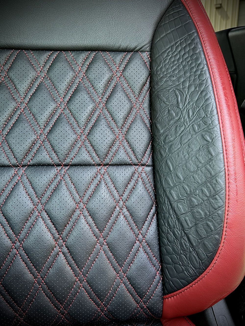 Close-up of a black car seat with diamond stitching, red accents, and textured side panel.