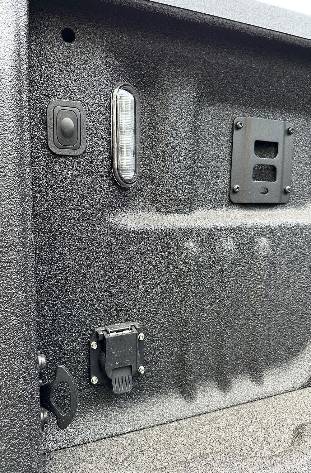 Black truck bed wall with various sockets, lights, and a trailer hitch.