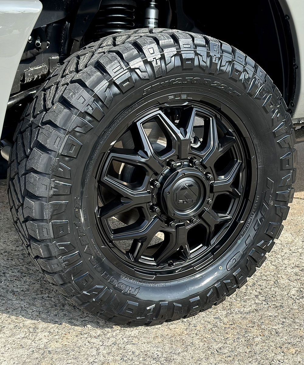 Black off-road truck tire and rim with a deep tread pattern, viewed at an angle.