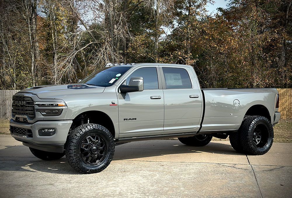 Gray lifted Ram truck with black wheels parked outside.