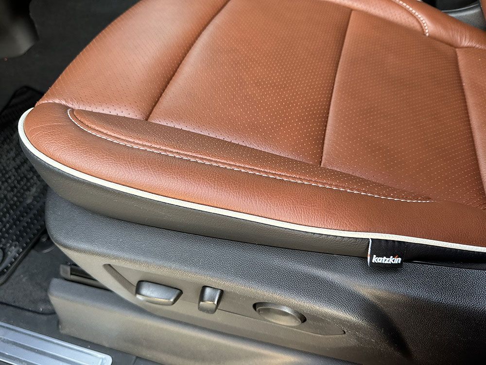 Brown leather car seat with white stitching and adjustment buttons.