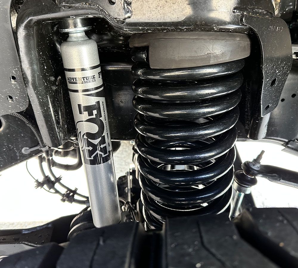 Close-up of a vehicle's suspension system: black coil spring, Fox shock absorber, and other metal components.
