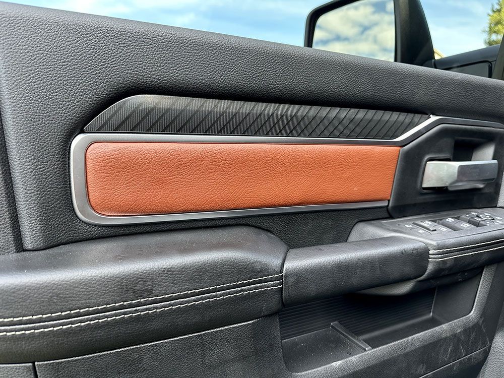 Close-up of a truck door panel with brown leather armrest, black textured trim, and chrome accents.