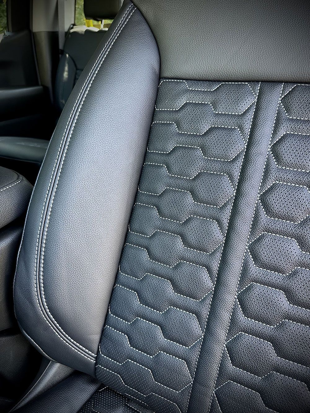Close-up of a car seat. Black leather with stitched geometric pattern. Gray stitching and trim.