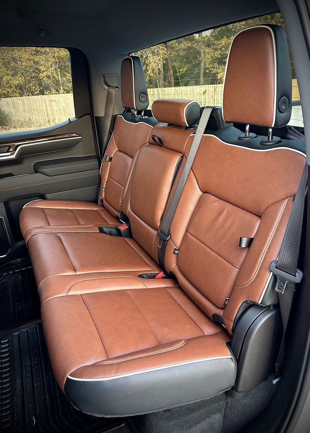 Brown leather truck backseat with headrests, seatbelts, and a center armrest.
