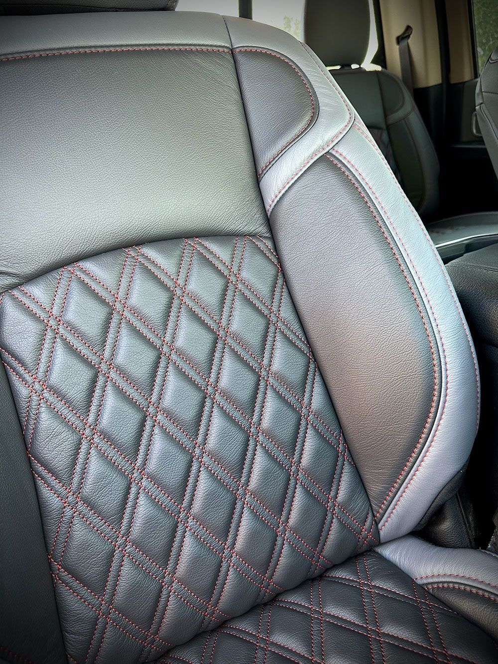 Close-up of a car seat with diamond-stitched gray and black leather with red stitching.