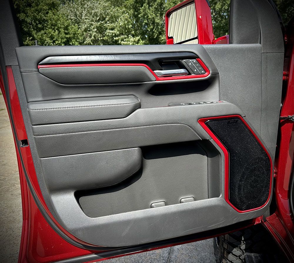 Red truck door panel with black and red trim, featuring speaker, storage, and armrest.