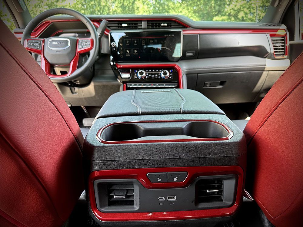 Interior view of a red and black GMC truck, showing dashboard, steering wheel, console, and rear air vents.
