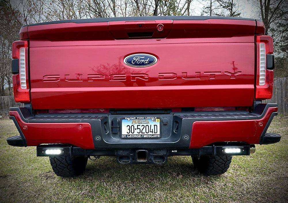 Red Ford Super Duty truck's rear, with bumper lights and a license plate, parked on grass.