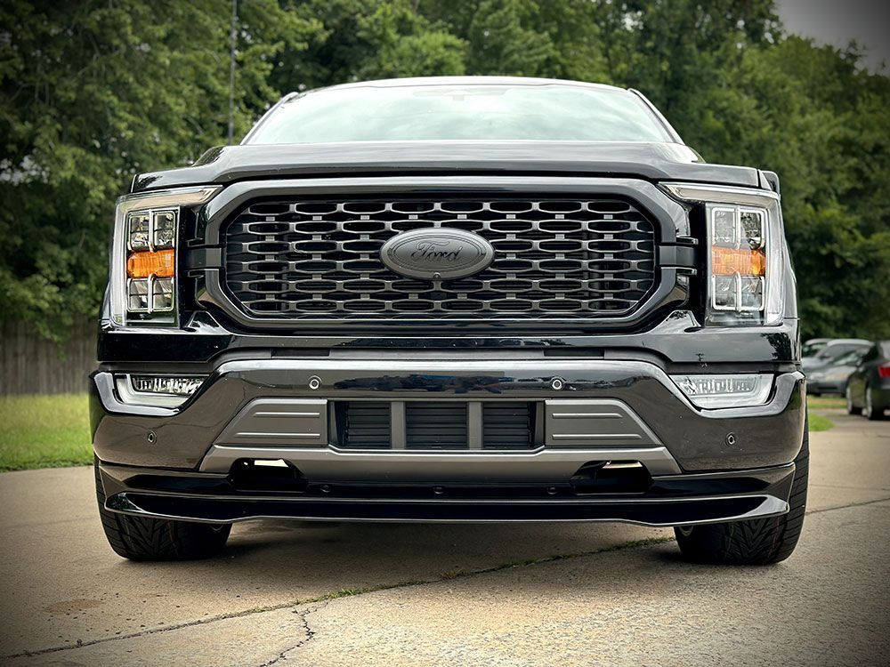 Black Ford F-150 truck, front view, in a driveway. Black grille, headlights, and bumper.