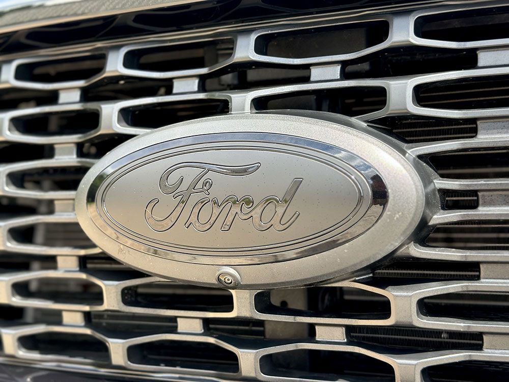 Close-up of a silver Ford emblem on a vehicle grille, with the word 