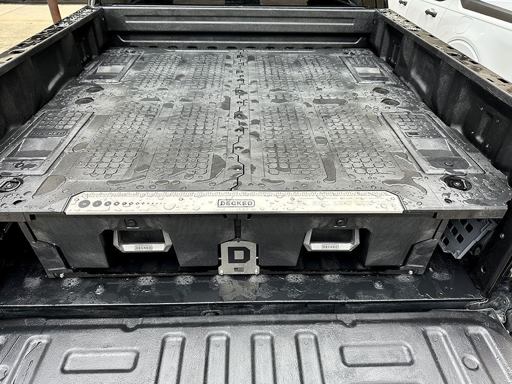A truck bed storage system in a pickup truck. The system is dark grey with two pull-out drawers.