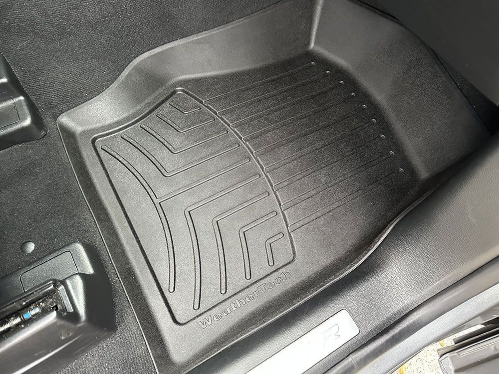 Black car floor mat with raised edges and textured surface, in a car.
