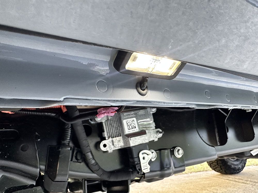 Undercarriage view with a light fixture illuminating a vehicle's electrical components, showing a small box and wiring.