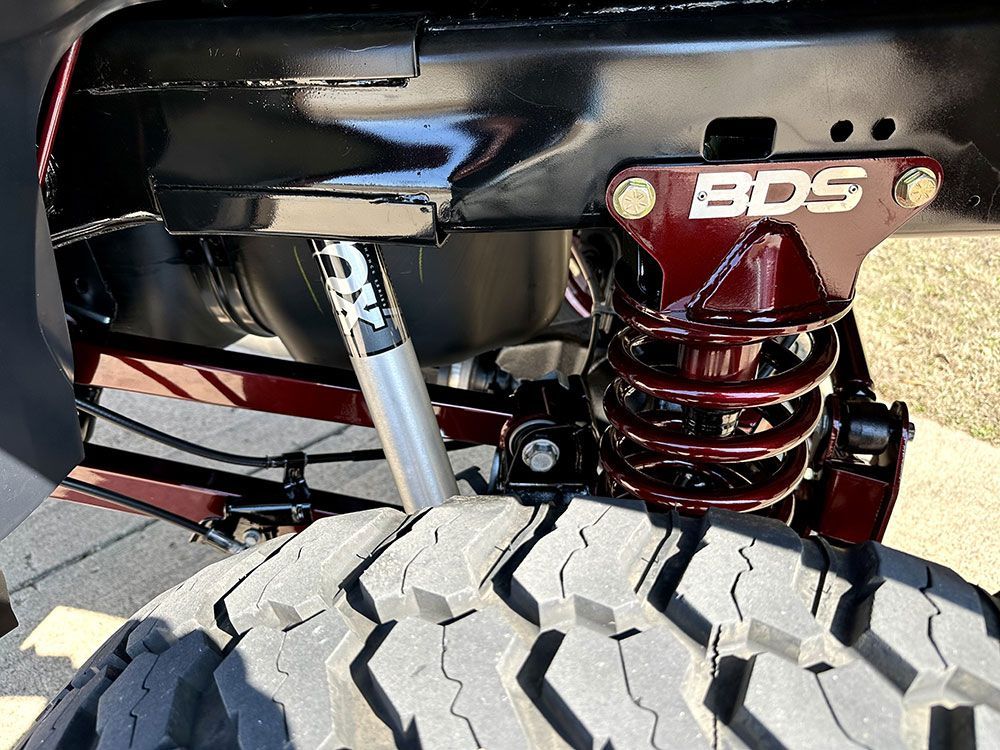 Close-up of a lifted truck suspension, showing a red BDS bracket, coil spring, and Fox shock absorber. Black and red details.