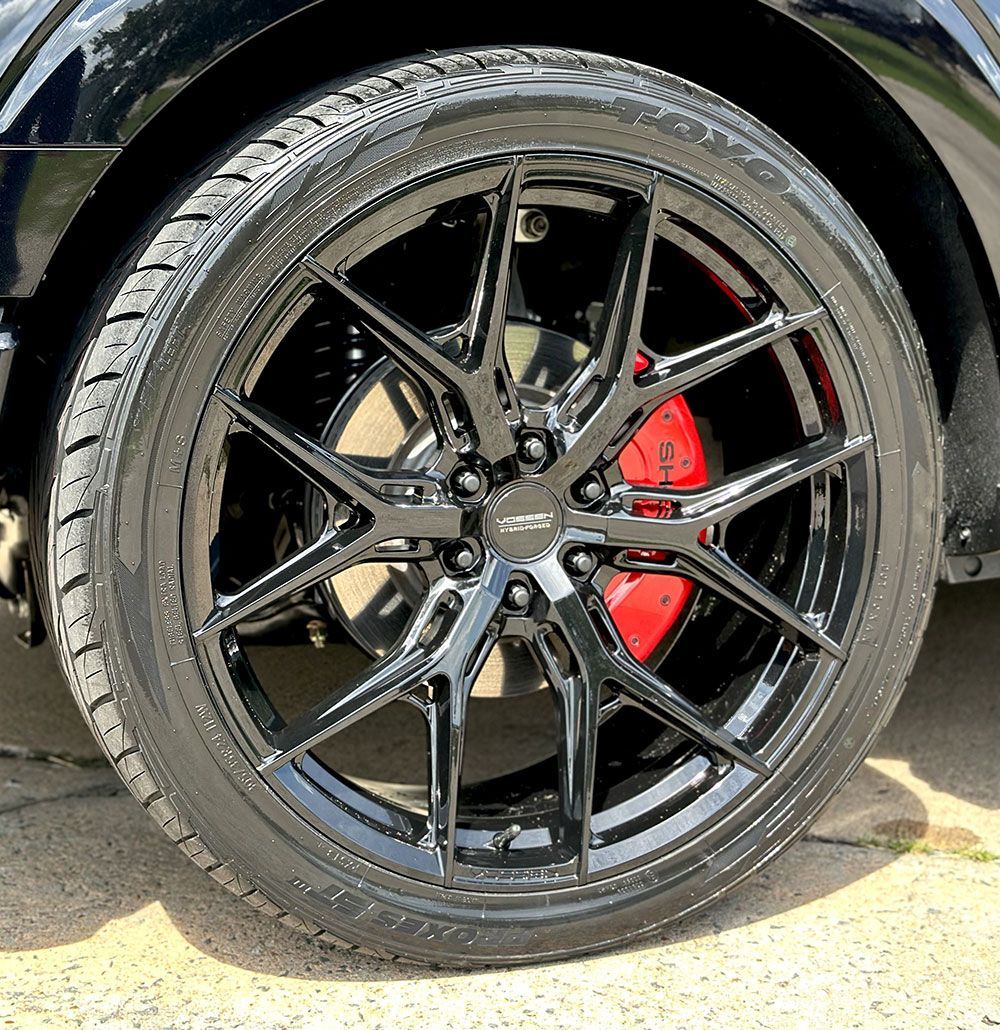 Black car tire with black rim and red brake caliper.