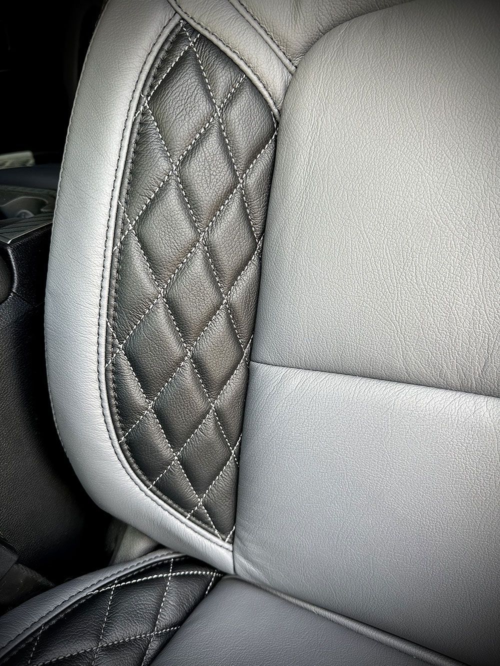 Close-up of a car seat with diamond-stitched black leather on the side and gray fabric.
