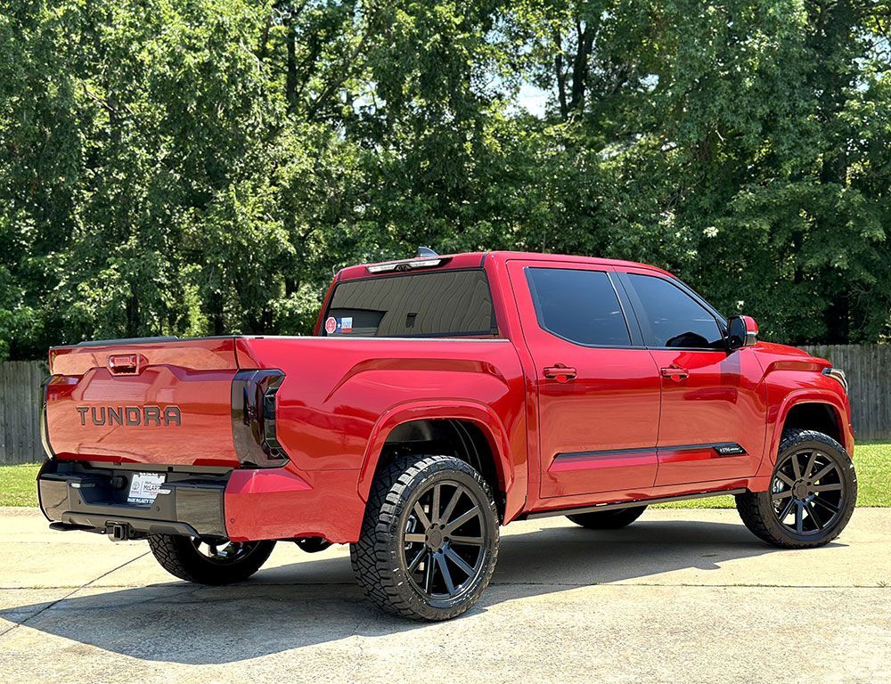 Red Toyota Tundra truck with black wheels and tinted windows parked on a concrete surface.