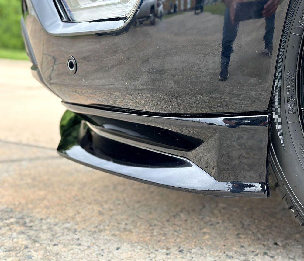 Black car's front bumper with a black lower spoiler, parked on asphalt.