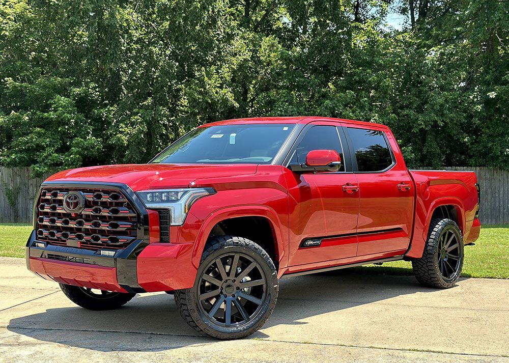 Red Toyota Tundra pickup truck with black wheels and grille, parked outdoors.