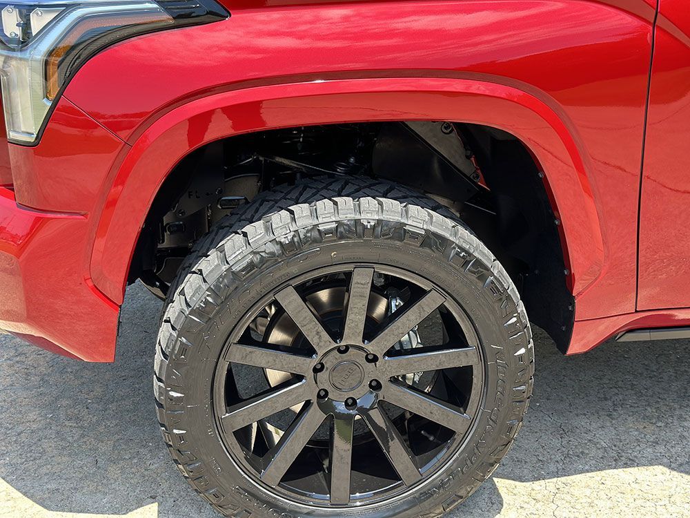Red truck's front wheel with black rim and tire. Close-up, outdoors.