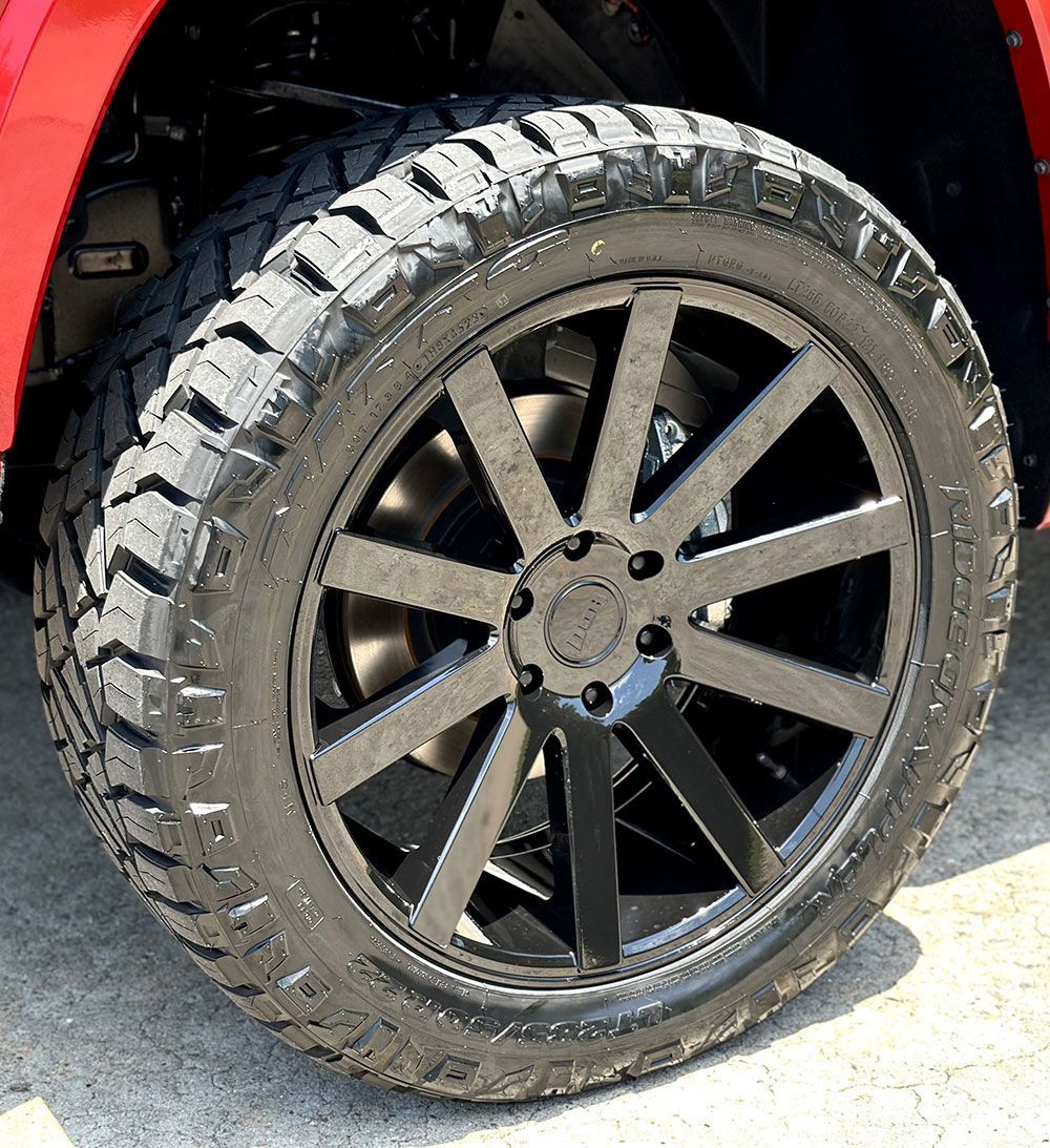 Black alloy wheel with all-terrain tire on a red vehicle.
