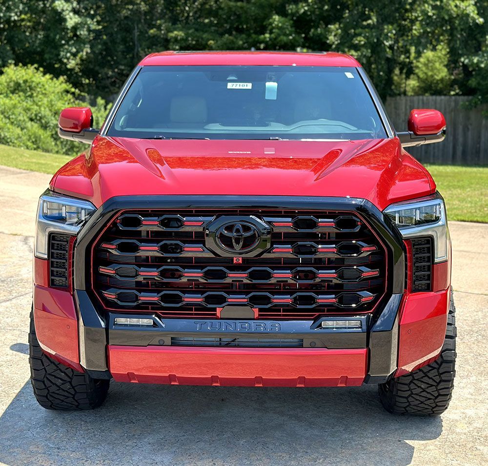 Red Toyota Tundra truck with a black and red custom grille and off-road tires, parked outdoors.
