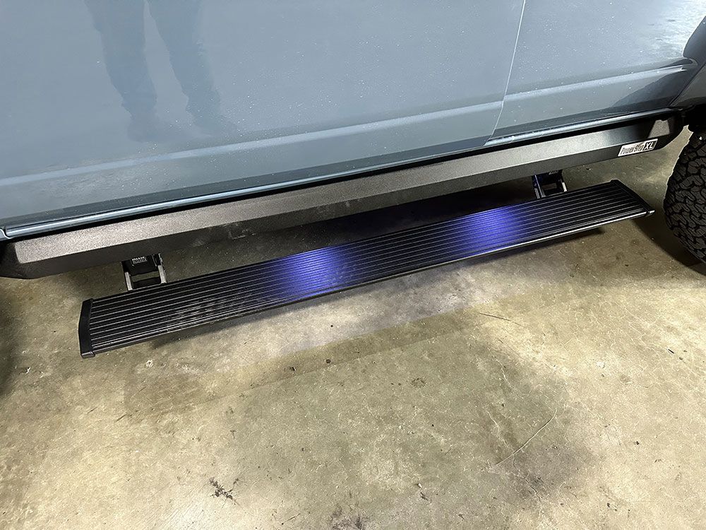 Black running board with blue under-glow lights installed on a gray vehicle.