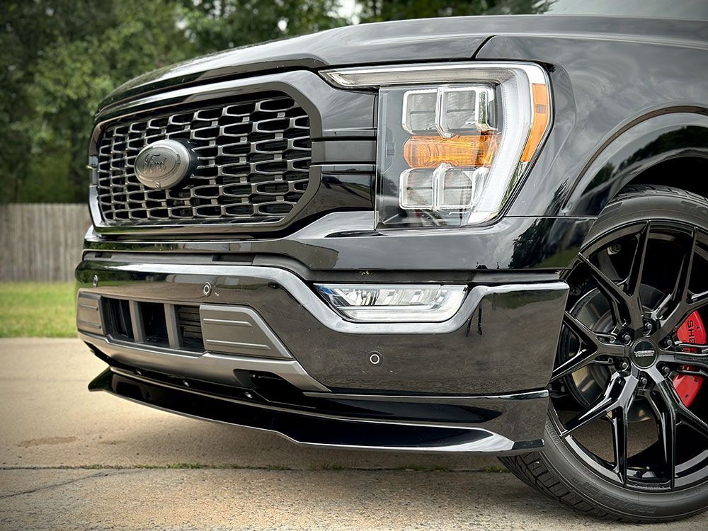 Black Ford F-150 truck front with custom grille, headlights, lowered stance, and black wheels with red calipers.