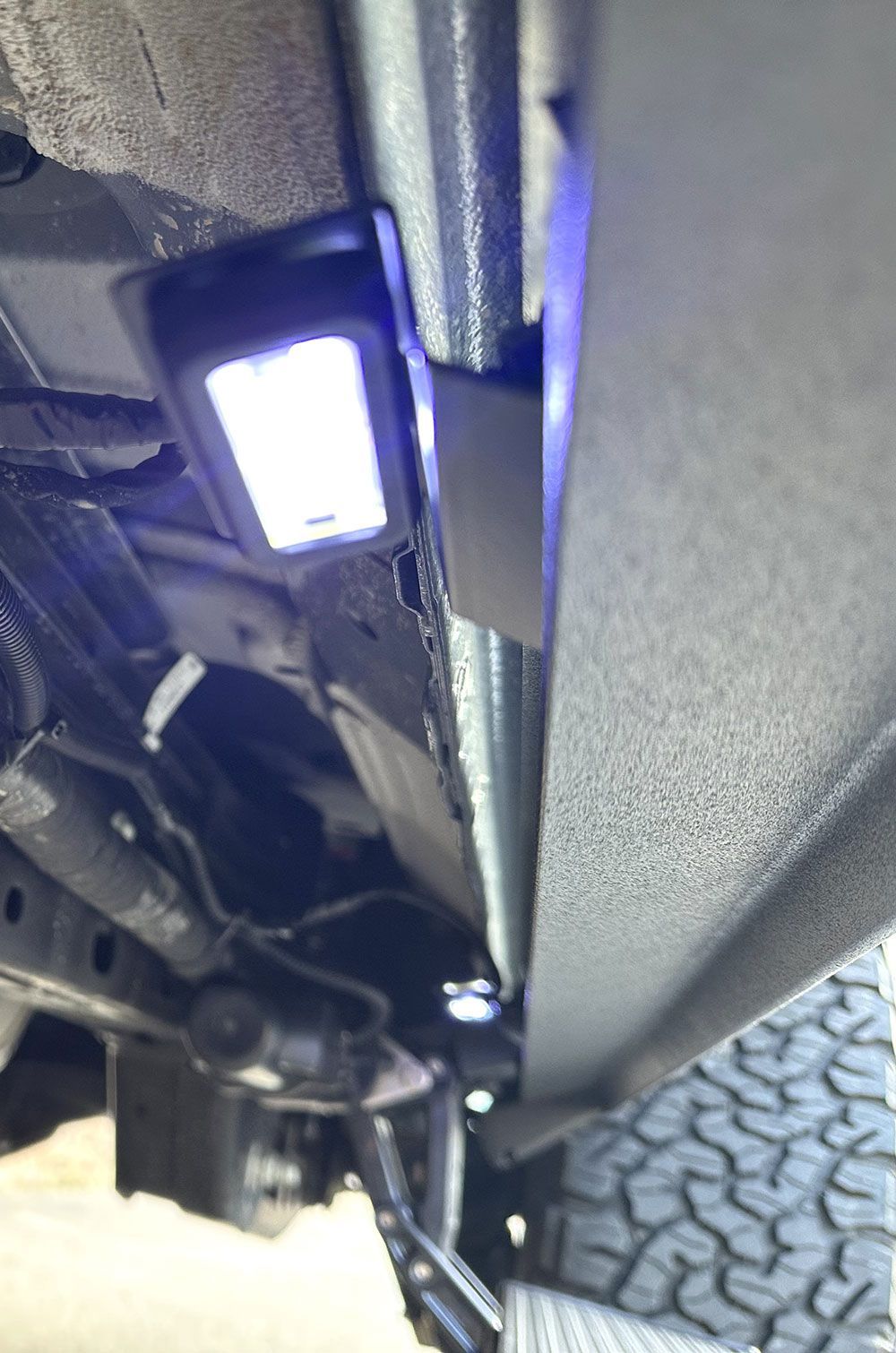Under-vehicle lighting, white light illuminates a small rectangular panel on a truck.