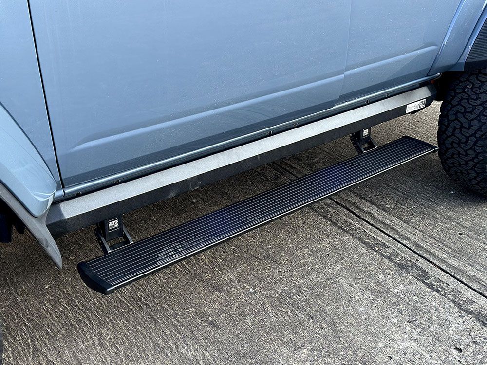 Side step on a blue vehicle. Black step with textured surface, mounted below the door.