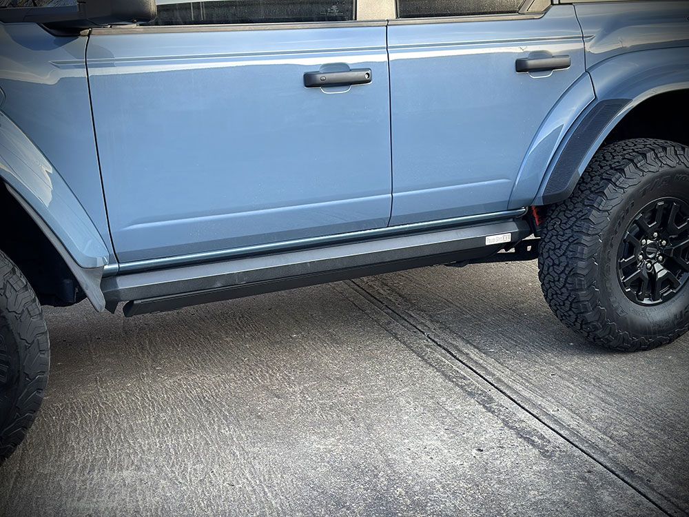 Blue Ford Bronco with black running boards and tires parked on concrete.