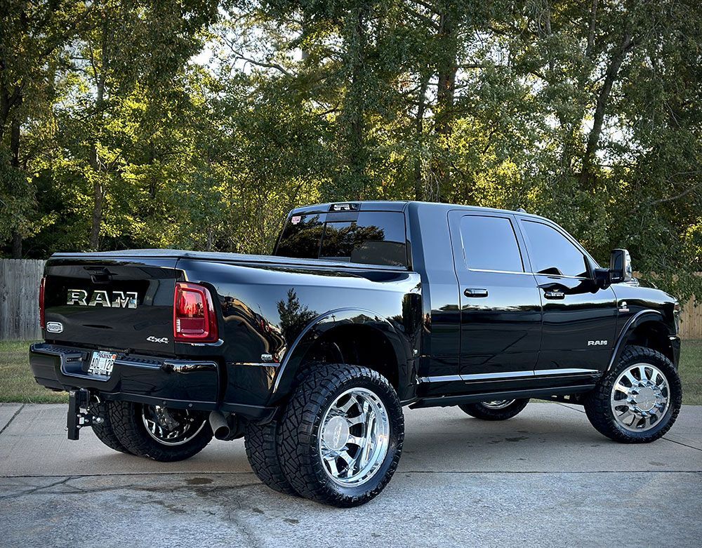 Black Ram dually pickup truck with large chrome wheels and tinted windows parked on a concrete surface.