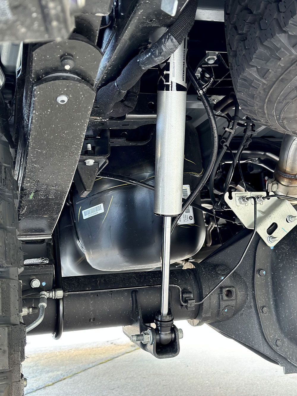 Undercarriage of a truck showing a shock absorber, suspension components, and a fuel tank.