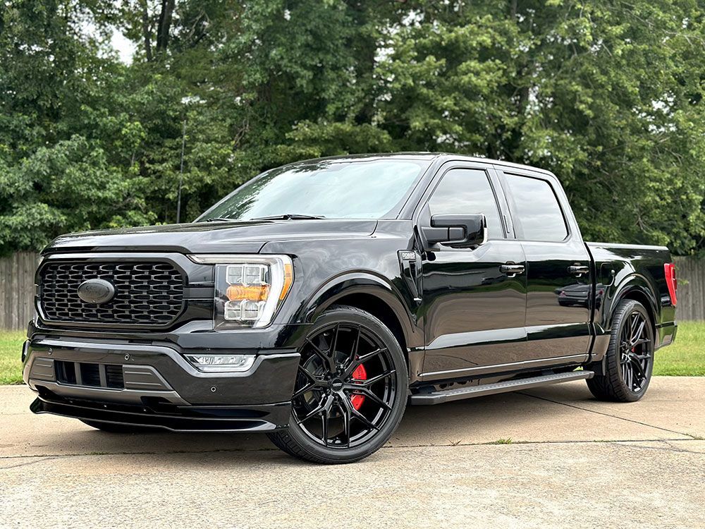 Black Ford F-150 pickup truck with custom black rims and red brake calipers parked outside, near trees.