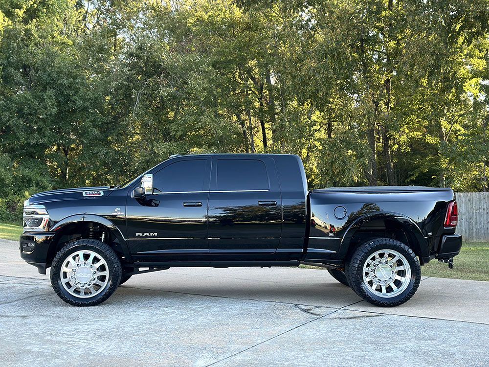 Black Dodge Ram pickup truck parked outdoors on a paved area, with tinted windows and chrome wheels.