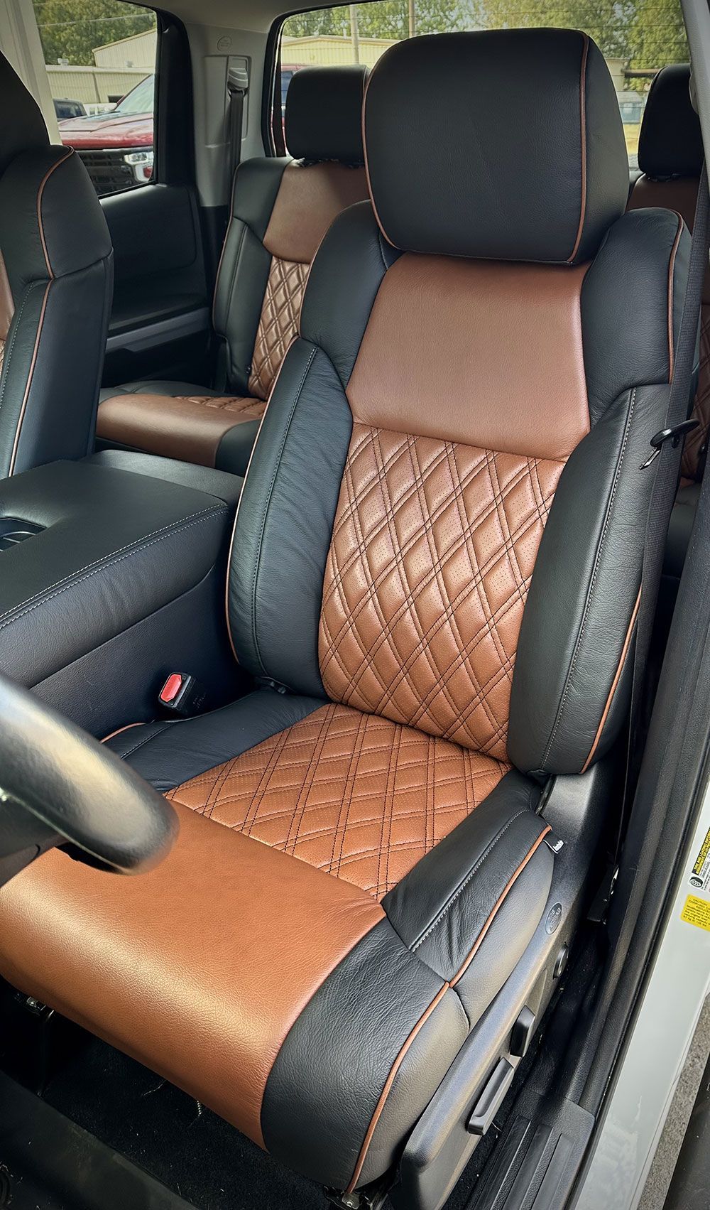Black and brown leather car seats with diamond stitching, featuring orange contrast stitching.