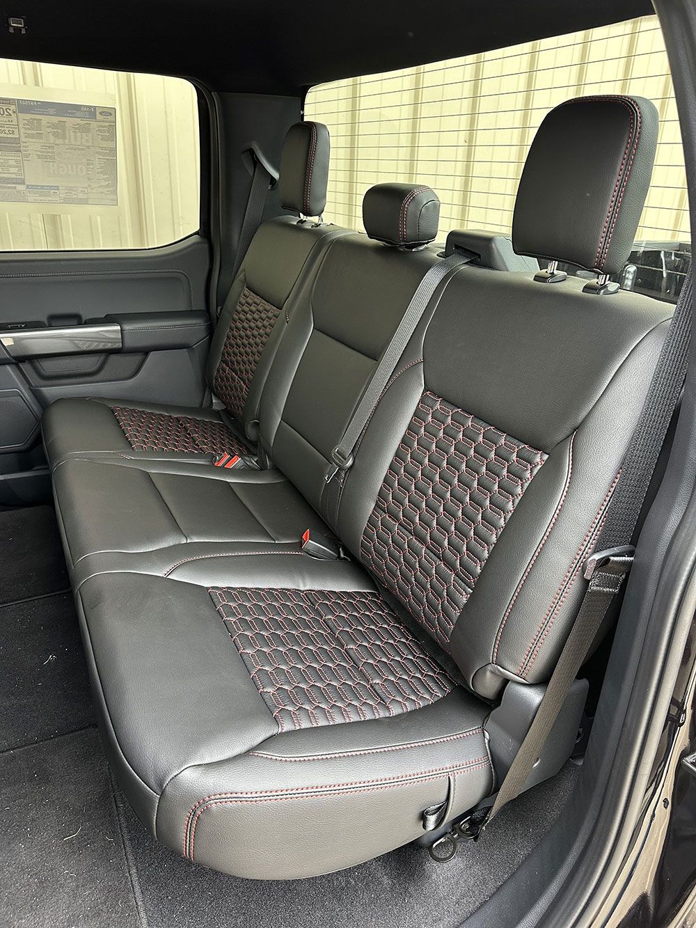 Backseat of a black truck with black leather seats, red stitching, and patterned center panels.