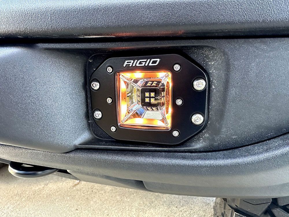Black LED light by Rigid mounted on a black vehicle bumper, emitting amber light.